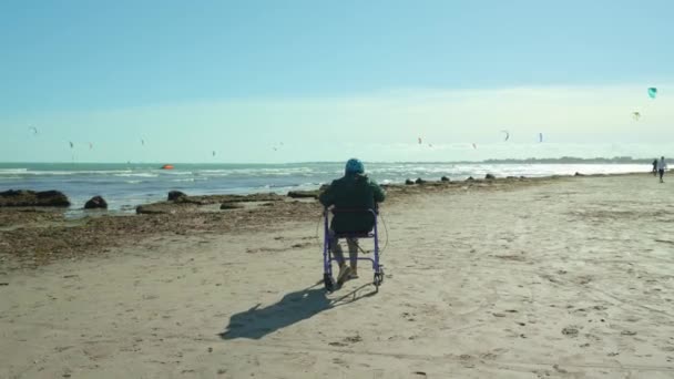 Öreg nő ül tolószék-rollator a velencei lagúna strandon — Stock videók