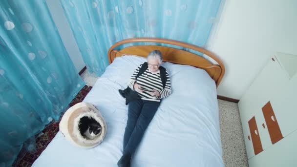 Avó com cabelos grisalhos lê notícias no tablet deitado no gato — Vídeo de Stock