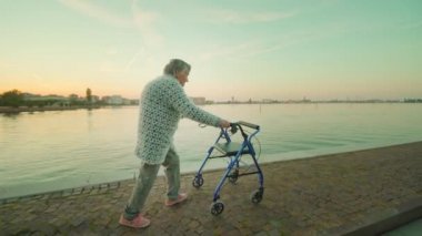 Yaşlı kadın, Venedik gölü yakınlarında Rollatör ile yolda yürüyor.