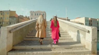 Moda kıyafetleri içinde genç bayan arkadaşlar köprü basamaklarında yürüyor.