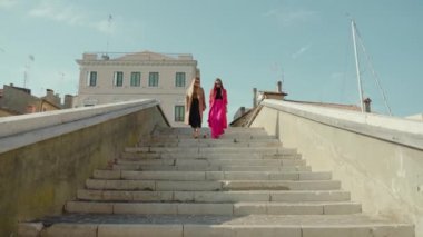 Parlak elbiseli genç kızlar köprüden aşağı iniyor.