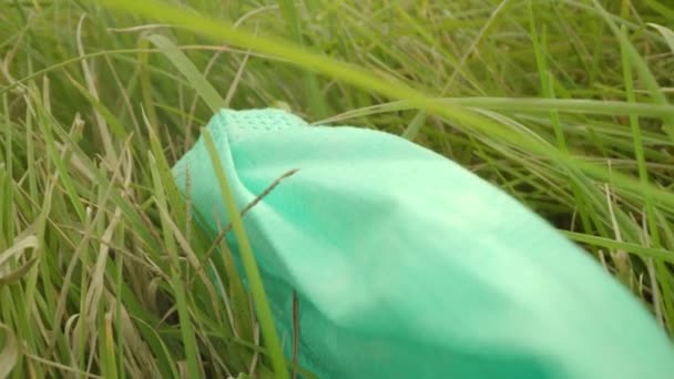Używana maska medyczna leżąca na zielonej trawie z suszonymi liśćmi — Wideo stockowe