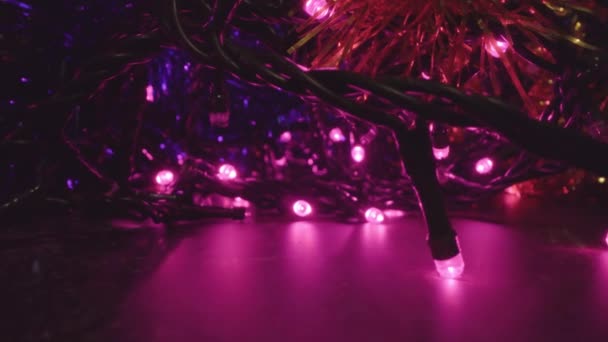 Luces de hadas púrpuras brillantes con oropeles en habitación oscura — Vídeo de stock