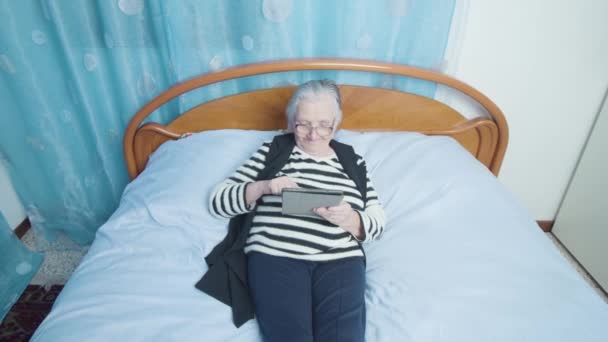 老年妇女在床上用平板电脑滚动社交媒体 — 图库视频影像