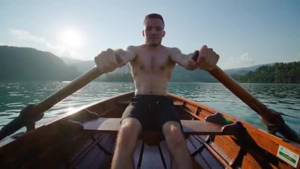 Молодий чоловік під час заходу вистрілює весла в дерев "яному човні на озері Блед. — стокове відео
