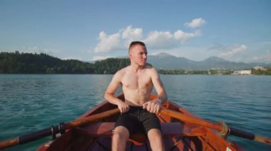 Genç adam, Bled Gölü 'ndeki tahta kayıkta kürekleri kontrol ediyor.