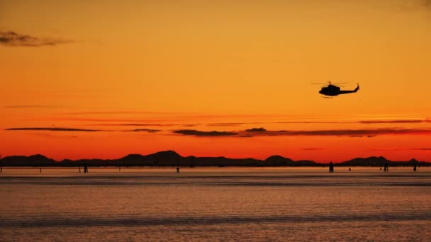 Helikopterin karanlık silueti nehrin üzerinde günbatımında uçuyor. — Stok video