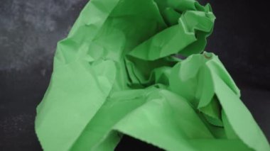 Motion to bright green crumpled paper on black table