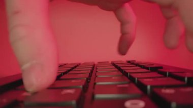 Person types fast on keyboard working at table on red