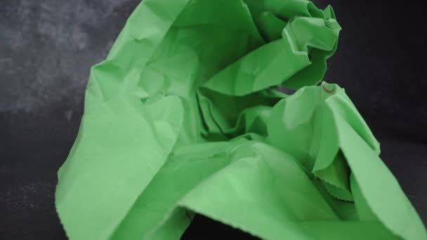 Κίνηση σε φωτεινό πράσινο τσαλακωμένο χαρτί σε μαύρο τραπέζι — Αρχείο Βίντεο