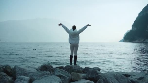 Mulher turista levanta as mãos de pé sobre rochas perto do lago Garda — Vídeo de Stock