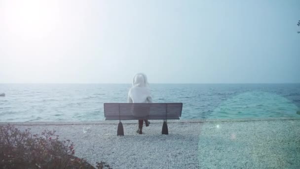 Mulher senta-se no banco solitário olhando para lago Garda com ondas — Vídeo de Stock