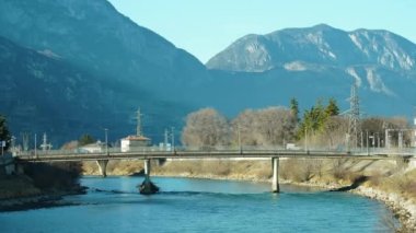 Trento 'da mavi nehir boyunca inşa edilen köprüde yoğun trafik sisli dev kayalık dağlara karşı. İtalya 'da güneşli bir sonbahar günü sona eriyor