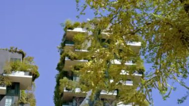 MILAN, İtalya - 10 Nisan 2022 Milano 'da popüler bir turizm merkezi olarak dikey orman evi. 10 Nisan 'da Milano' da mavi gökyüzüne karşı balkonlarda ağaçları ve yeşillikleri olan yüksek binalar inşa edildi.