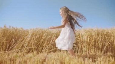 Cheerful girl with long loose hair runs in golden wheat field against clear blue sky. Happy kid enjoys sunny day in countryside slow motion