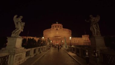 ROME, ITALY - MAY 12 2022: People walk on footbridge leading to Castel Sant Angelo at night. Huge mausoleum with statues of angels illuminated by lights in Rome on May 12 in Rome
