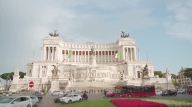 Cars and buses drive on road against Altar of Fatherland under cloudy sky. Historical building with statues on top attracts tourists in Rome