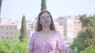 Young woman in glasses stands against large Colosseum building in Rome on sunny day. Female tourist enjoys summer vacation in Italy closeup