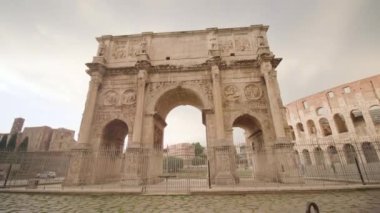 Ancient triumphal arch built against Colosseum in Rome in cloudy morning. Historical architecture in center of touristic Italian capital