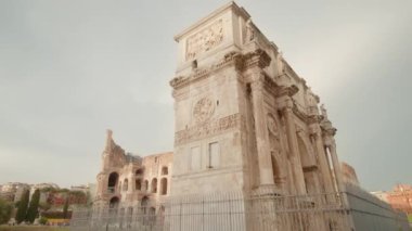 Triumphal arch built against Colosseum in center of Rome under cloudy sky. Historical architectural heritage of Italian capital low angle shot