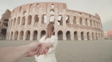 Woman holds hand of man walking to large Colosseum in Rome. Tourist couple explores architecture of Italian capital closeup slow motion