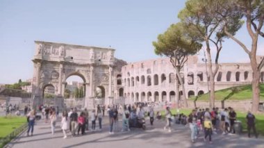 Tourists walk near Triumphal arch built near Colosseum in historical center of Rome. People explore ancient landmarks of Italy on sunny day