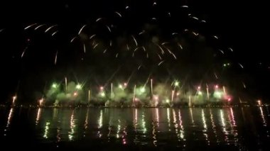 Colorful fireworks launched in air over city reflect on water surface at night. Bright glitter in dark sky on Feast of Redeemer in Venice
