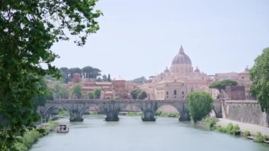 Saint Angelo bridge built over river against St Peter Basilica of Vatican. Ancient architecture of cathedral and nature on sunny summer day in Rome