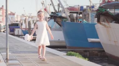 Girl walks in front of fishing boats with a basket in her hand in the city of Chioggia