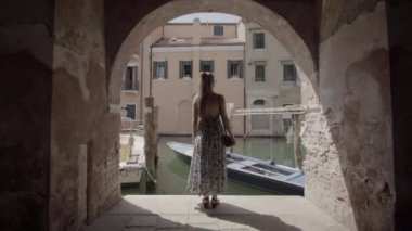Woman looks at canal with boats under arcades in Venice