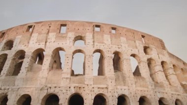 Ancient Colosseum stands in center of Rome against cloudy sky. Imposing amphitheater as historical monument of Italian city close low angle shot