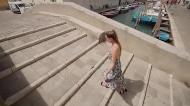 Woman with elegant dress walks on the bridge through Chioggia canal with boats