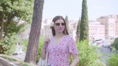 Woman in glasses holds backpack standing against ancient Colosseum on sunny day. Female traveler enjoys summer vacation in Rome closeup