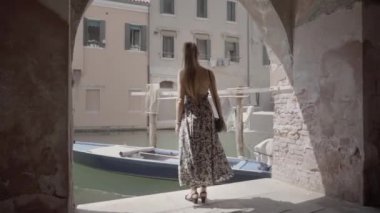 Woman with elegant dress stops under houses in Venice