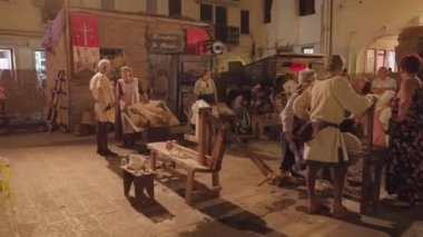 CHIOGGIA, ITALY - 18 Ağustos 2022: İnsanlar akşamları Chioggia 'nın aydınlık caddesine konulan ahşap süslemelerin yanında dururlar. İtalya 'da ortaçağ bayramının kutlanması 18 Ağustos' ta Chioggia 'da