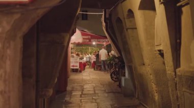 CHIOGGIA, ITALY - 18 Ağustos 2022: Chioggia 'daki ışıklarla aydınlatılmış eski taş binalar arasındaki dar yol. İnsanlar 18 Ağustos 'ta Chioggia' da Marciliana etkinliğini kutlamak için sokak kafesinde oturuyorlar.