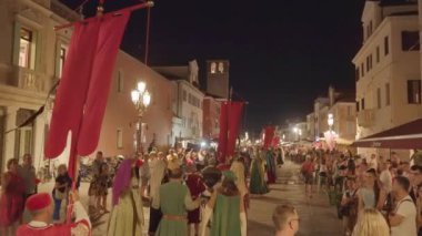 CHIOGGIA, İtalya - 18 Ağustos 2022: Ortaçağ kostümlü ve geceleri sokaklarda pankartlarla yürüyen insanlar. Ortaçağ Marciliana etkinliğinin geleneksel kutlaması 18 Ağustos 'ta Chioggia' da