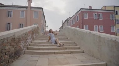 Genç bir kadın yazın Venedik 'in tarihi köprüsünde oturuyor.