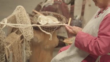 Yaşlı kadın, arka planda ahşap bir sopa kullanarak beyaz iplik dokuyor. Marciliana festivali için antik ekipmanlar