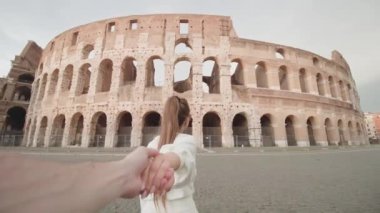 Adam bulutlu gökyüzüne karşı Roma 'daki antik Kolezyum' a doğru yürüyen kadını takip ediyor. Turist çift İtalya 'nın tarihi mimarisinin keyfini çıkarıyor.
