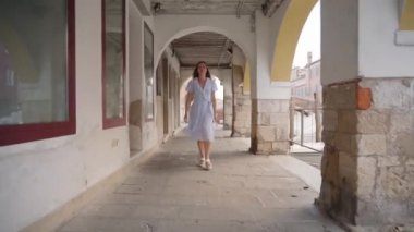 Genç ve güzel bir kadın, kanalın yakınındaki Venedik atari salonlarında teknelerle yürüyor.