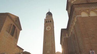 Güneş, açık mavi gökyüzüne karşı Duomo 'nun çan kulesinin arkasında parlıyor. İtalyan kasabasının eski binaları alçak açılı çekimle tarihi mimari