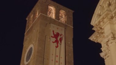 CHIOGGIA, ITALY - 18 AĞUSTOS 2022: Marciliana bayrağı karanlık gökyüzüne karşı Aziz Andrew Kule Saatine asılı. 18 Ağustos 'ta Chioggia' da eski İtalyan kasabasının aydınlanmış mimarisi.