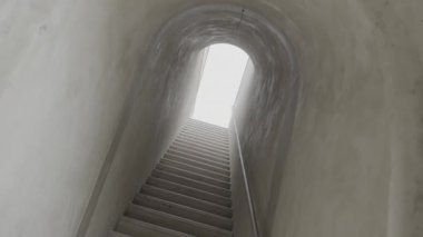 Parlak ışık, gri duvarları ve tırabzanlı taş merdivenleriyle uzun tünelleri aydınlatır. Girişinde güneş ışığı olan eski bir yeraltı yapısı.