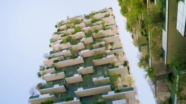 MILAN, İtalya - 10 Nisan 2022 Milano 'da mavi gökyüzüne karşı dikey orman gökdelenleri. 10 Nisan 'da Milano' da yeşil ağaçlı ve balkonlu kuleler ve çalılar alçak açılı çekimler yapıldı.