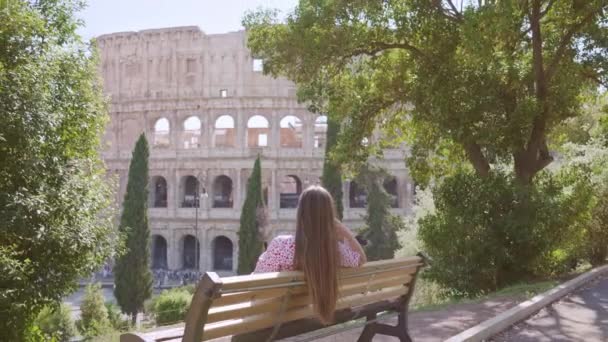 Mujer Sienta Banco Mirando Antiguo Coliseo Detrás Exuberantes Árboles Verdes — Vídeos de Stock