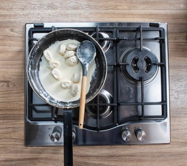 Ev mutfağında hamur tatlısı. Tavada kaynamış hamur köftesi. Arka plan olarak çiğ donmuş hamur köfteleri, üst manzara. Ev yemeği.