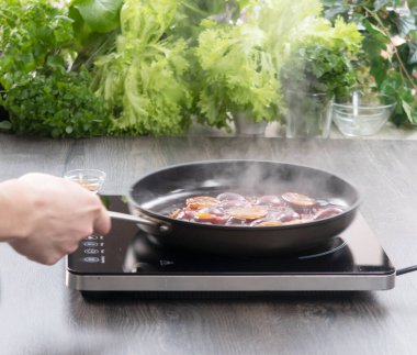 Elektrikli ocağın üstünde tava. Adamın eli elektrikli ocakta sebze pişiriyor..