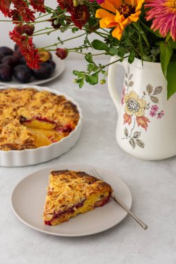 Badem taneli ev yapımı erik keki, vazoda sonbahar çiçekleri, tabakta bir dilim kek.
