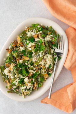 Kavrulmuş badem gevreği, yeşil fasulye, riccotta peyniri ve mozzarella, yeşil soğanlı sebze salatası ve oval bir tabakta maydanoz.